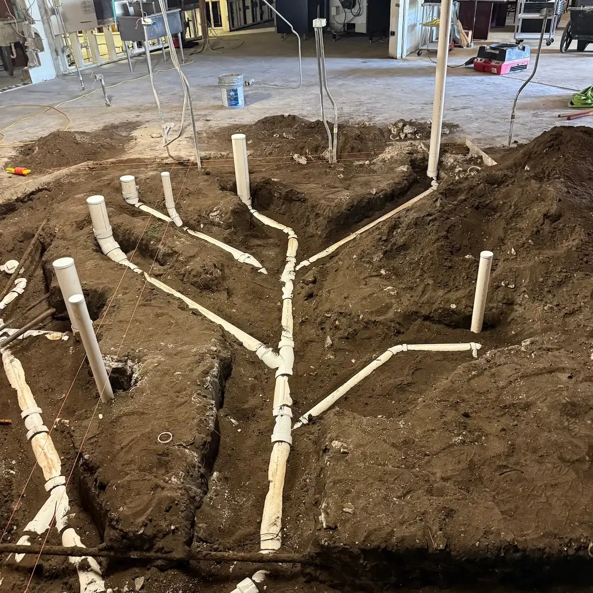 Ground-level view of heavy commercial underground PVC waste and sewer piping laid down inside trenches prior to concrete pouring.